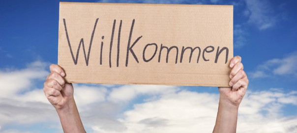 Hände halten ein Schild mit dem handgeschriebenen Wort Willkommen.